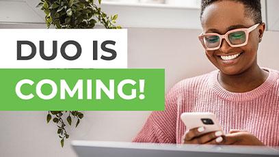 photo of a female smiling with on her phone using Duo to log into the laptop in front of her.
