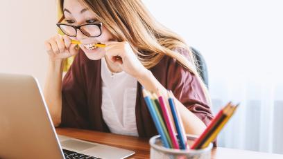 Woman biting pencil as she studies on laptop