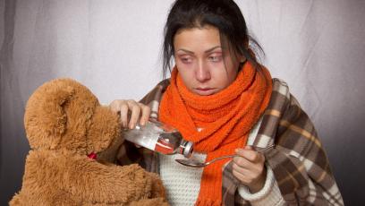 Young woman, sick, taking cough syrup while looking at teddy bear