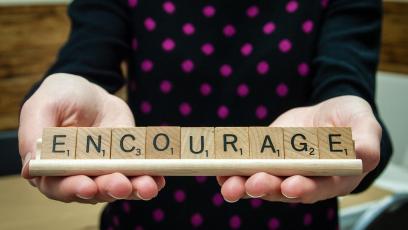 A pair of hands holding up Scrabble tiles spelling ENCOURAGE