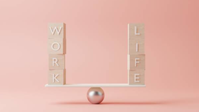 Two sets of word tiles spelling "WORK" and "LIFE" balancing on a beam atop a metal ball
