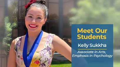 Kelly Sukkha, a Rio Salado College student, smiles outside in the sunlight wearing a floral dress and a blue medallion. A graphic overlay reads: “Meet Our Students – Kelly Sukkha, Associate in Arts, Emphasis in Psychology.” The background shows a modern building with windows and greenery.