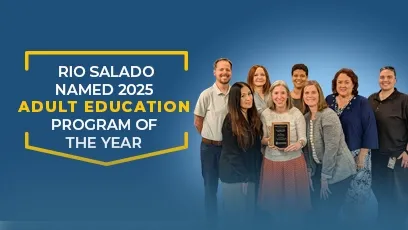 A group of Rio Salado College staff members stand together smiling, with one person in the center holding a plaque. The background features a blue gradient with white and yellow text that reads: “Rio Salado Named 2025 Adult Education Program of the Year.” The team poses proudly, representing the college’s award-winning adult education program.