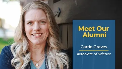 Carrie Graves, a blonde woman with long wavy hair, smiles while standing outdoors next to a dark wooden wall. She is wearing a navy blazer over a light blue top and layered necklaces. A blue graphic box on the right reads: ‘Meet Our Alumni — Carrie Graves, Associate of Science.’