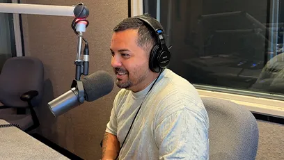 Frank Nino IV in the recording studio during his podcast interview. He is wearing a gray shirt and headphones, smiling.