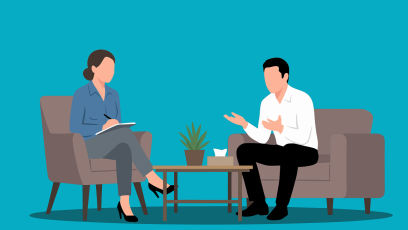 A man speaking to a woman therapist; both of them are seated with a table between them with a potted plant on it. Behind them is a solid aquamarine blue background