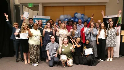 Group photo of approximately 20 Rio Salado College educator preparation program completers and staff posing indoors in front of blue and white balloons. Several individuals are holding certificates, and banners for the Educator Preparation Program are visible in the background. Participants are arranged in rows, smiling and facing the camera during a recognition event.