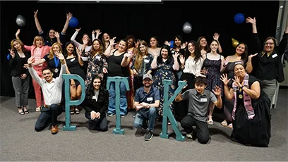 Large group of newly inducted Phi Theta Kappa members posing together on stage behind large “PTK” letters during the 2026 induction ceremony.