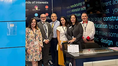 **Alt text:** Six professionals stand together smiling at a conference exhibit booth during an education and workforce event.
