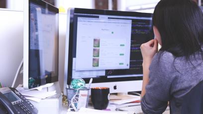 Woman in office working on two computer monitors
