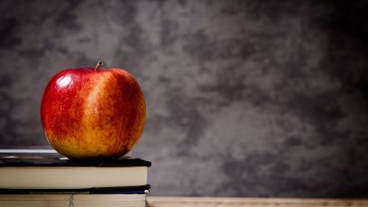 An apple on a stack of books in front of a chalkboard