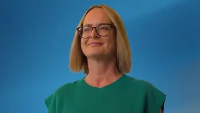 Alt text: Amy Gentry smiles while wearing glasses and a green top, posed against a blue background.