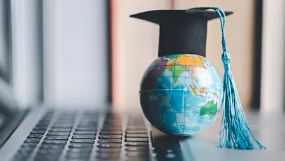 A globe next to a keyboard wearing a graduation cap