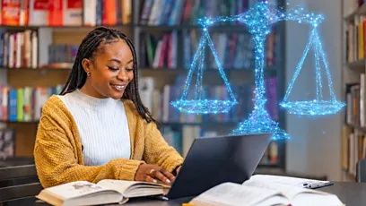 A smiling woman with long braids wearing a mustard-yellow cardigan works on a laptop at a library table with open textbooks. A glowing blue digital illustration of the scales of justice appears above the laptop, representing legal studies and online education.