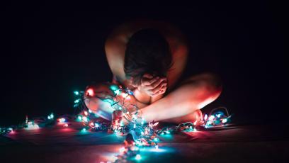 Stressed woman sits on the floor surrounded by Christmas lights