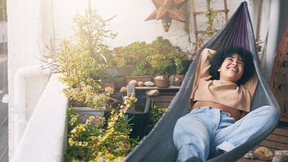 woman in a hammock on a balcony, surrounded by plants, taking a break