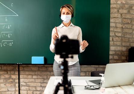 Teacher presenting in front of a chalkboard and video camera.