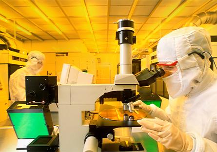 Technician using microscope to inspect silicon wafer with computer chips in production cleanroom.