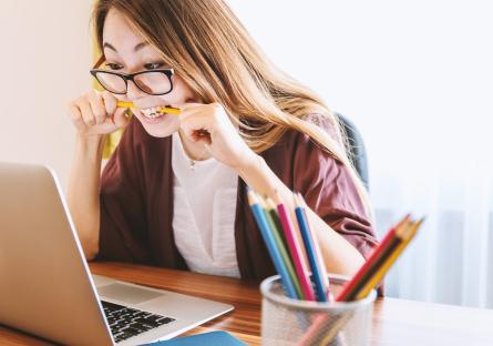 Woman biting pencil as she studies on laptop