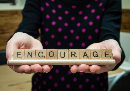 A pair of hands holding up Scrabble tiles spelling ENCOURAGE