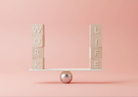 Two sets of word tiles spelling "WORK" and "LIFE" balancing on a beam atop a metal ball