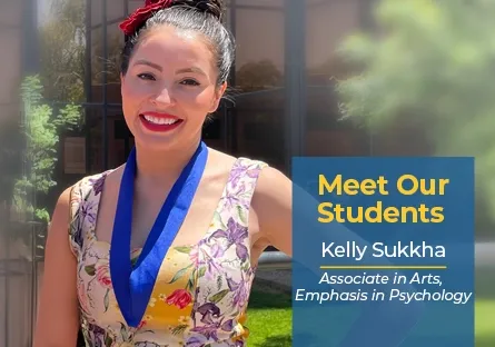 Kelly Sukkha, a Rio Salado College student, smiles outside in the sunlight wearing a floral dress and a blue medallion. A graphic overlay reads: “Meet Our Students – Kelly Sukkha, Associate in Arts, Emphasis in Psychology.” The background shows a modern building with windows and greenery.