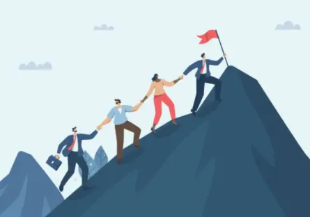 A group of people in business clothes holding hands as they climb a mountain while their leader plants a flag on the summit