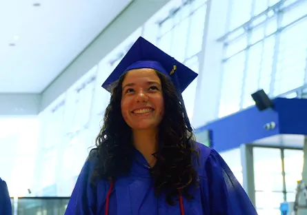 Alexandria Woodruff smiles while wearing a blue graduation cap and gown inside the Desert Financial Theater