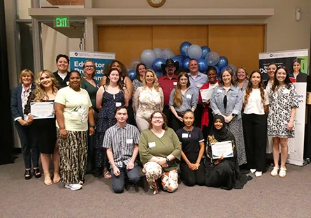 Group photo of approximately 20 Rio Salado College educator preparation program completers and staff posing indoors in front of blue and white balloons. Several individuals are holding certificates, and banners for the Educator Preparation Program are visible in the background. Participants are arranged in rows, smiling and facing the camera during a recognition event.