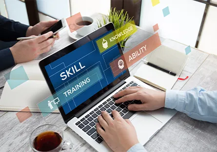 Person typing on a laptop at a desk with a phone, notebook, and coffee nearby, with overlay text reading “Skill Training,” “Knowledge,” and “Ability.”