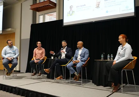 Panelists speak on stage during a discussion at a professional conference.