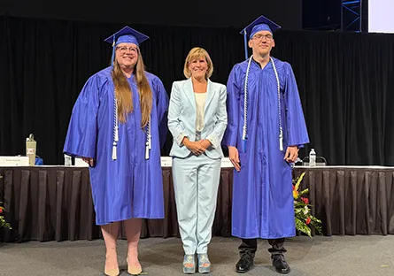 Rio Salado College President Dr. Kate Smith stands with student speakers Brianna Reynolds and Joseph Rogers, who are wearing blue graduation caps and gowns, on a commencement stage.