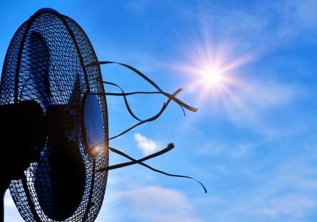 A fan blowing air outdoors under a hot sun