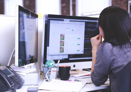 Woman in office working on two computer monitors