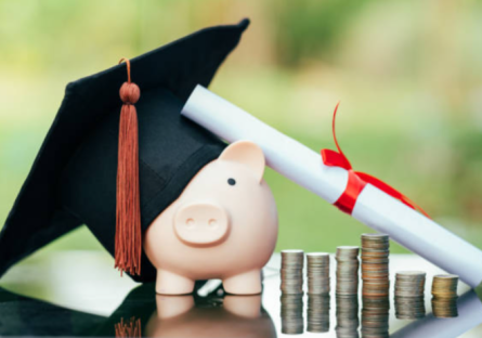 A piggybank wears a graduate's cap next to a diploma and stacks of coins