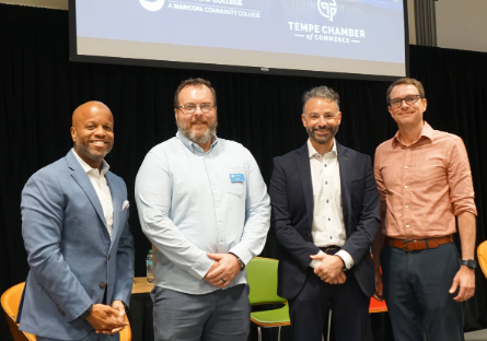Four panelists stand together smiling on stage following a professional discussion.