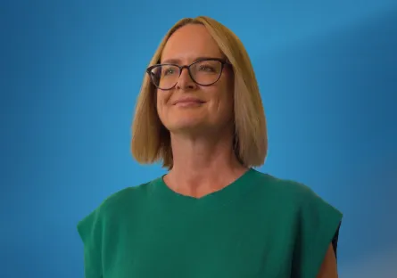 Alt text: Amy Gentry smiles while wearing glasses and a green top, posed against a blue background.