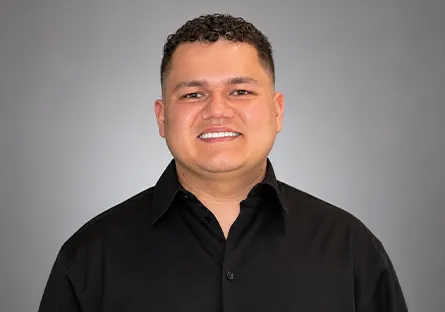Portrait of Yeison Ramirez Mendez smiling at the camera in a black button-down shirt against a neutral gray studio background.