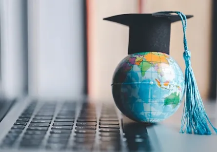 A globe next to a keyboard wearing a graduation cap
