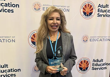 Veronica Gutierrez smiles while holding her AALL Support Staff of the Year award in front of an Arizona Department of Education Adult Education Services backdrop.