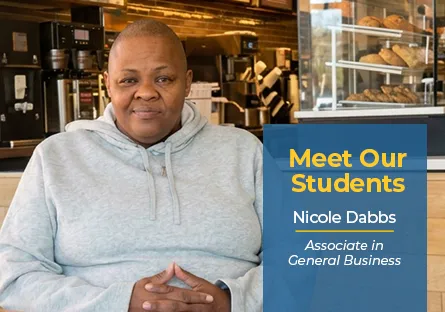 Nicole Dabbs sits inside a café wearing a gray hoodie. A blue graphic beside her reads, “Meet Our Students, Nicole Dabbs, Associate in General Business.”