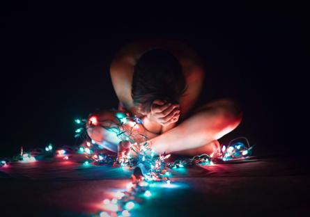 Stressed woman sits on the floor surrounded by Christmas lights