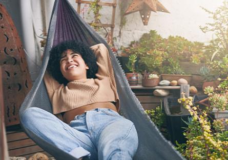 woman in a hammock on a balcony, surrounded by plants, taking a break