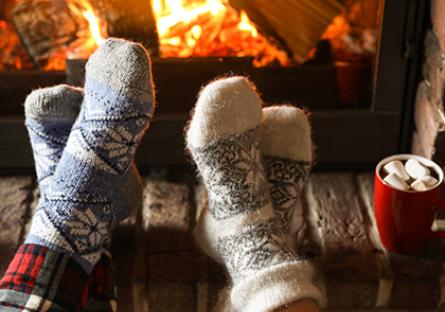 two pairs of feet wearing wooly socks in front of fire with hot cocoa