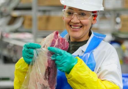 Female JBS employee packing meat. Smiling at camera