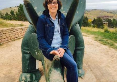 photo of Sarah Stohr sitting on a dinosaur statute with the desert in the background