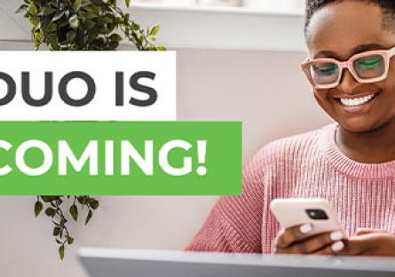 photo of a female smiling with on her phone using Duo to log into the laptop in front of her.