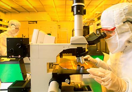 Technician using microscope to inspect silicon wafer with computer chips in production cleanroom.