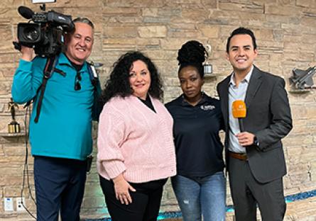 photo of news reporter and camera posing with student and faculty chair