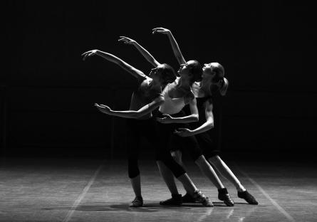 Three ballerinas dancing in a black and white photo